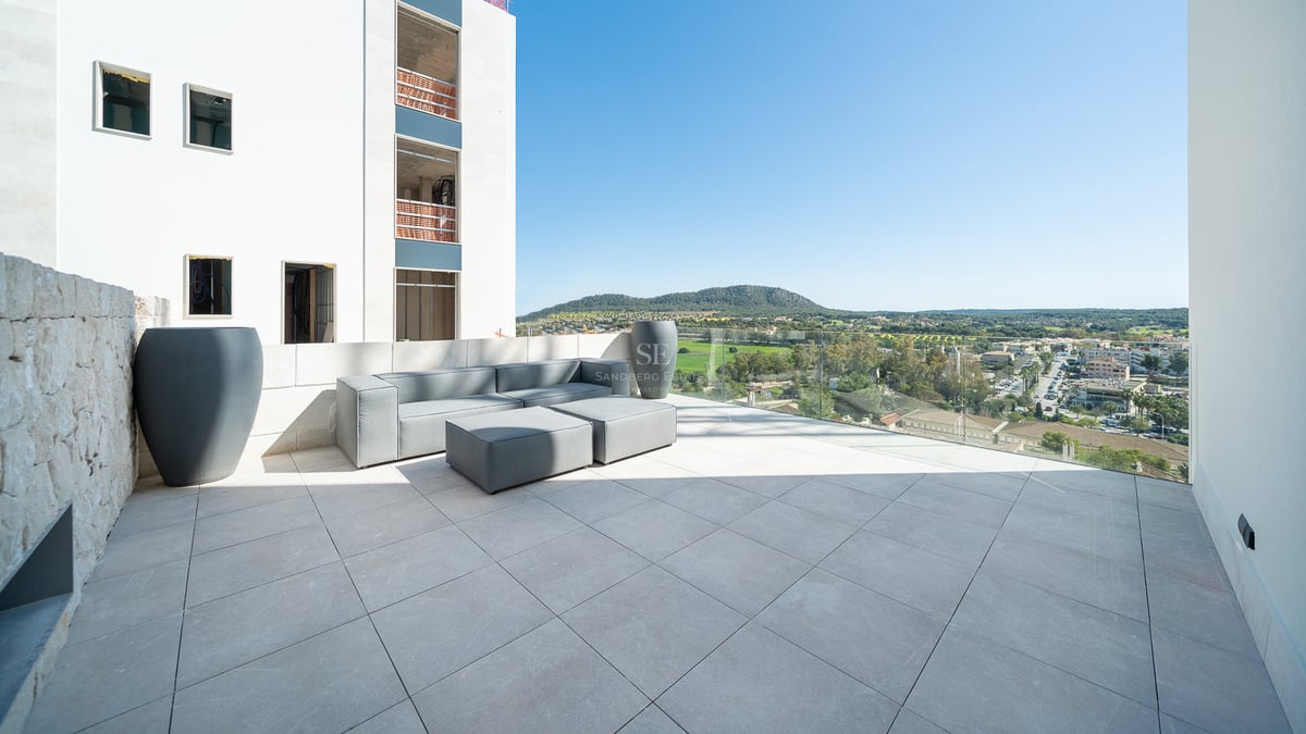 Terrasse au design épuré avec canapé gris, garde-corps en verre et vue sur le paysage naturel.