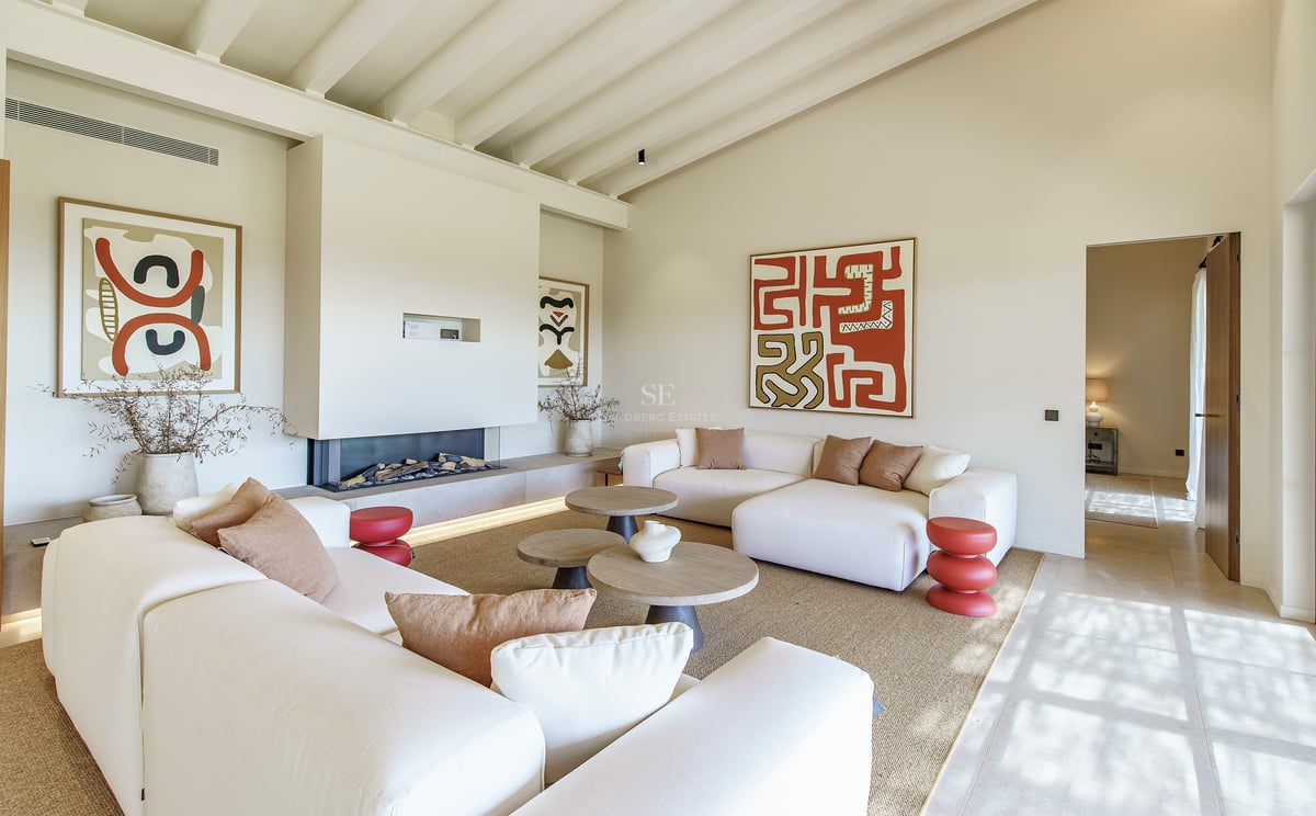 Helles Wohnzimmer mit hohen Balkendecken, modernem Kamin, weißen Sofas und abstrakter Wandkunst.