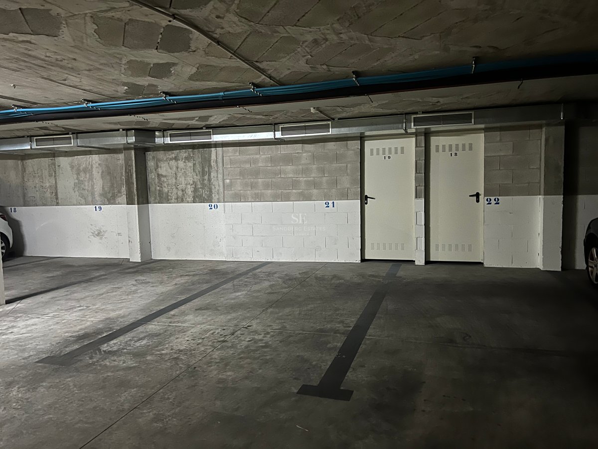 Garage souterrain avec sol en béton, places numérotées et portes de rangement en métal blanc.