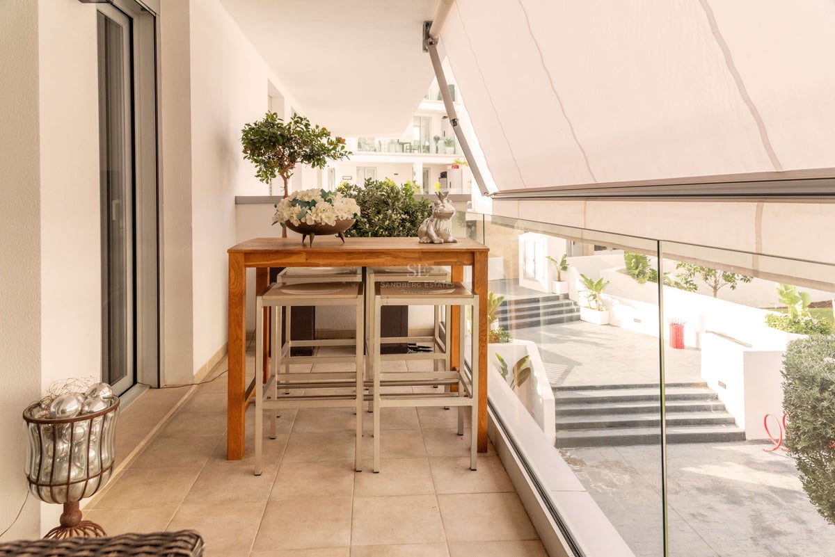 Moderne Terrasse mit hohem Holztisch, Hockern, weißer Markise und Glasgeländer mit Blick auf den Innenhof.