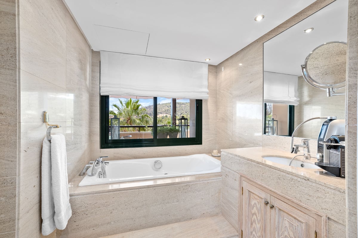 Salle de bain principale élégante avec baignoire en pierre, grande fenêtre avec vue et vasque en marbre.