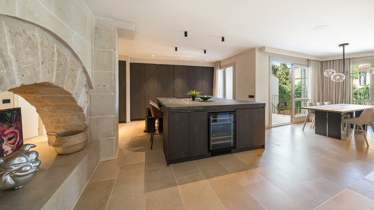 Cuisine haut de gamme avec îlot sombre, cave à vin, arche en pierre naturelle et salle à manger lumineuse.