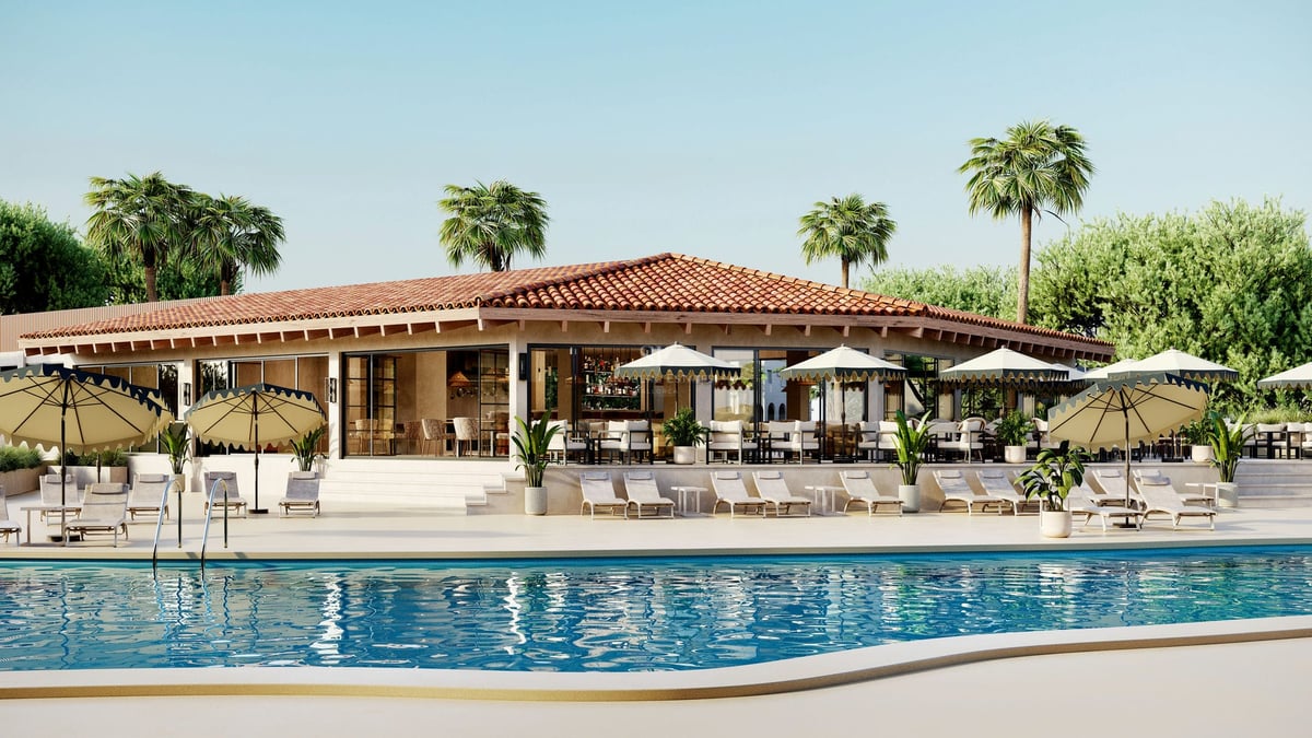 Grande piscine bleue avec chaises longues et parasols devant un bâtiment de style méditerranéen avec des palmiers.