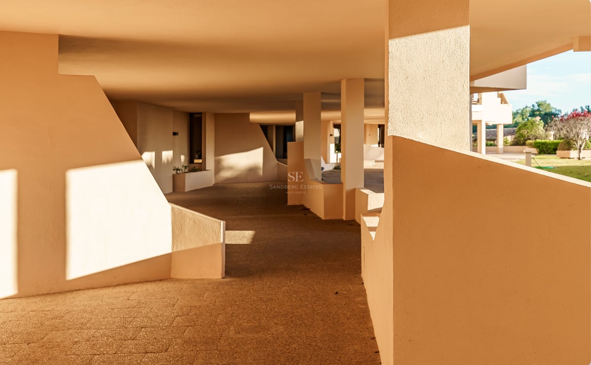 Schattiger Außenweg mit beigen geometrischen Wänden und Steinboden bei warmem Sonnenlicht und scharfen Schatten.