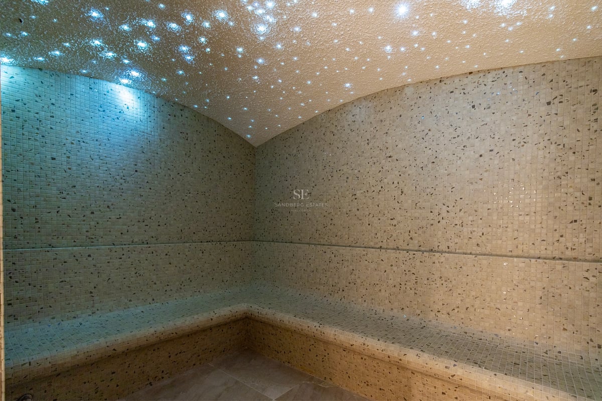 Hammam de luxe avec mosaïque beige et plafond en fibre optique effet ciel étoilé.