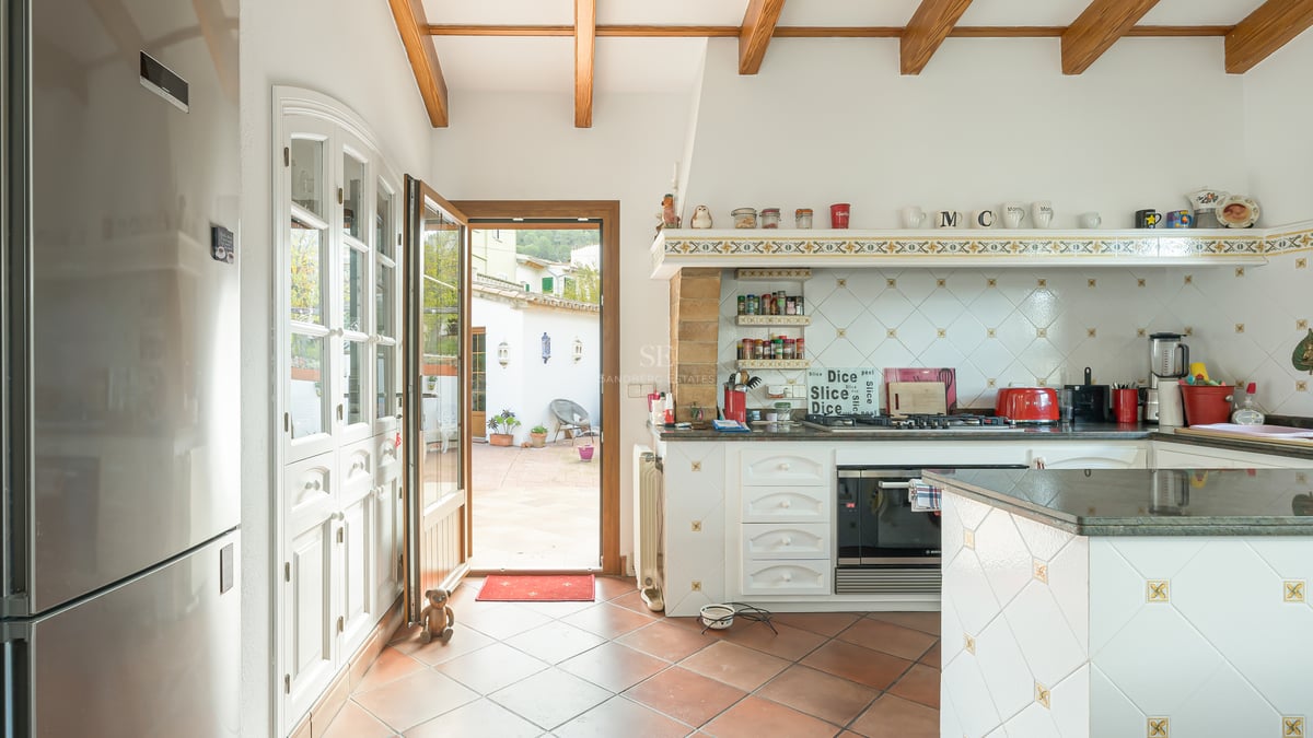 Kitchen featuring exposed wood beams, terracotta floors, and an open door leading to a sunny courtyard.