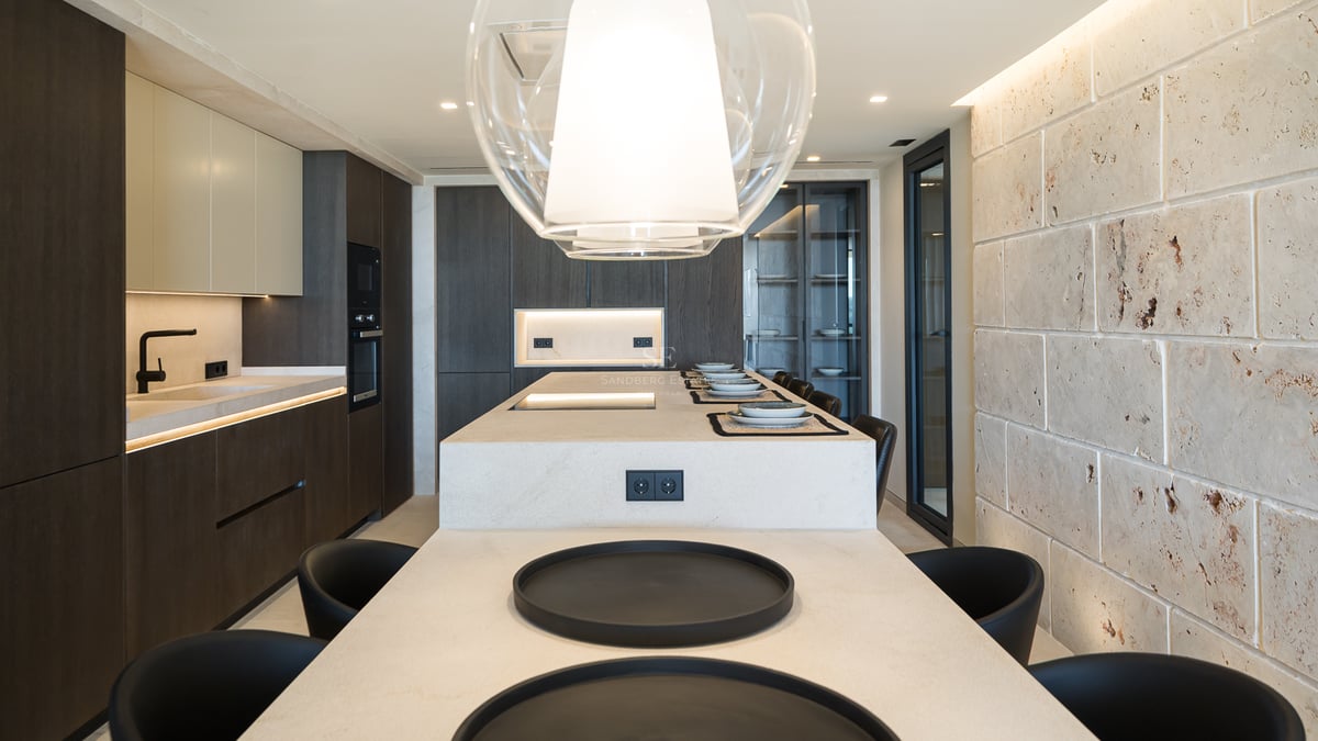 Cuisine moderne avec un grand îlot en pierre, des armoires en bois sombre et un mur en pierre naturelle texturée.