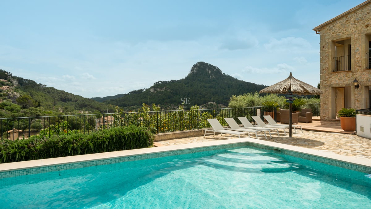 Piscine extérieure avec chaises longues sur une terrasse en pierre, surplombant un paysage de montagne verdoyant.