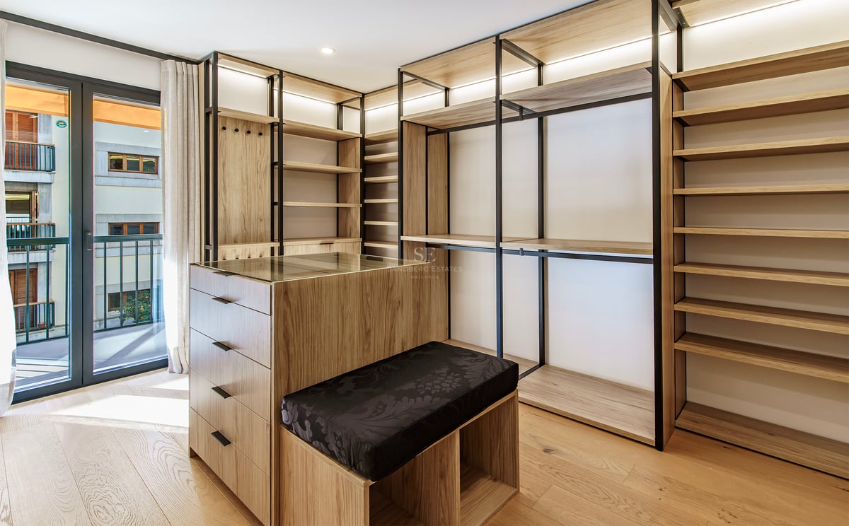 Dressing moderne avec étagères en bois clair, cadres en métal noir, un îlot central et accès au balcon.