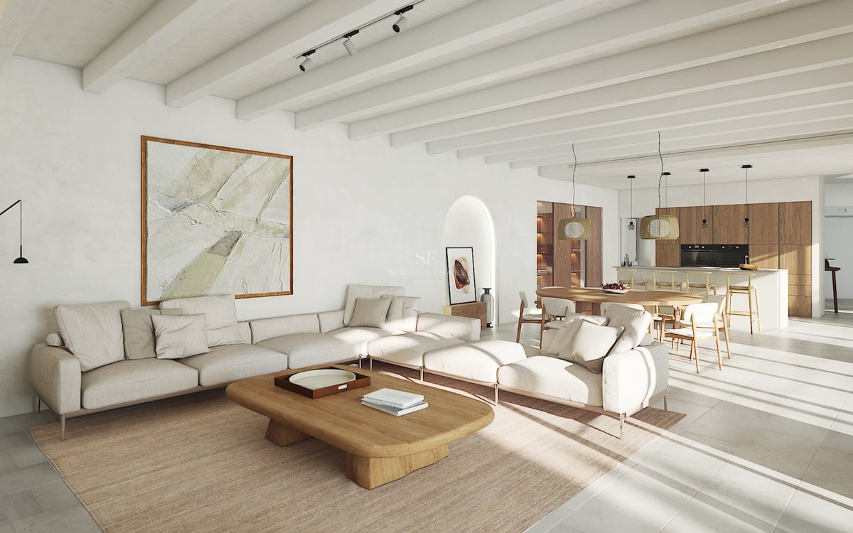 Salon lumineux à aire ouverte avec poutres blanches, canapé modulaire, table en bois et cuisine intégrée.