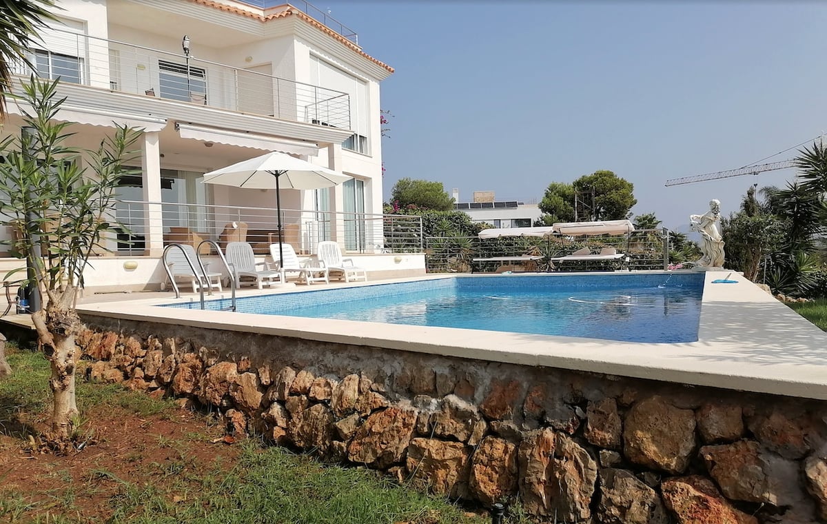 Piscine privée avec chaises longues devant une villa blanche aux murs en pierre naturelle.