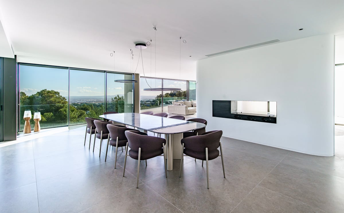 Salle à manger moderne élégante avec une grande table, des chaises sombres et des baies vitrées donnant sur la nature.