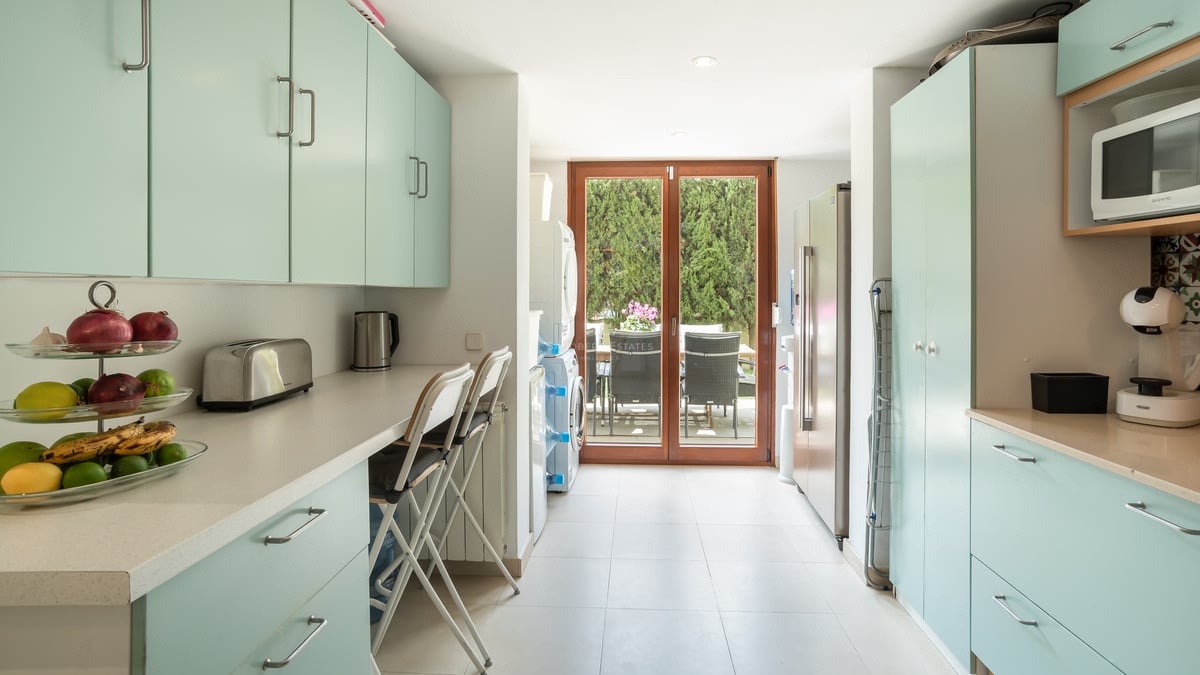 Cuisine lumineuse avec placards vert menthe, plans de travail blancs, coin buanderie et accès au patio verdoyant.