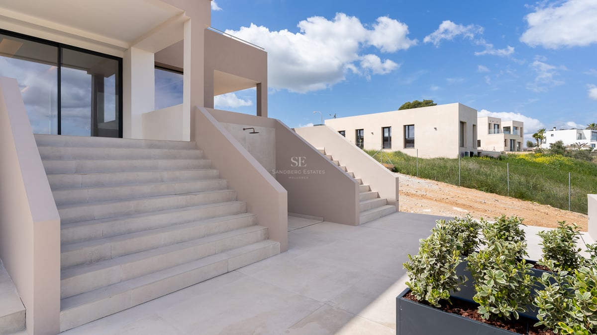 Moderne Natursteintreppen führen zu einer beigen Villa unter strahlend blauem Himmel.