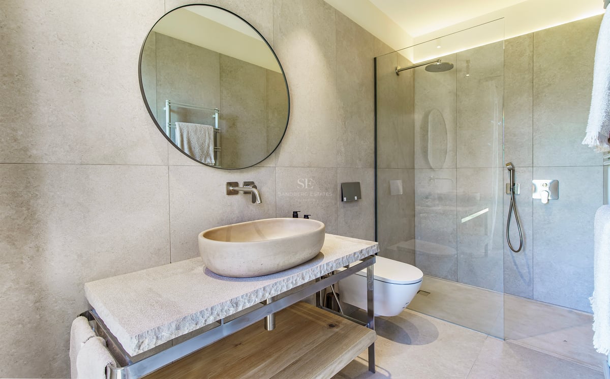 Modernes Badezimmer mit ovalem Steinbecken, Rundspiegel und begehbarer Glasdusche mit großen Fliesen.