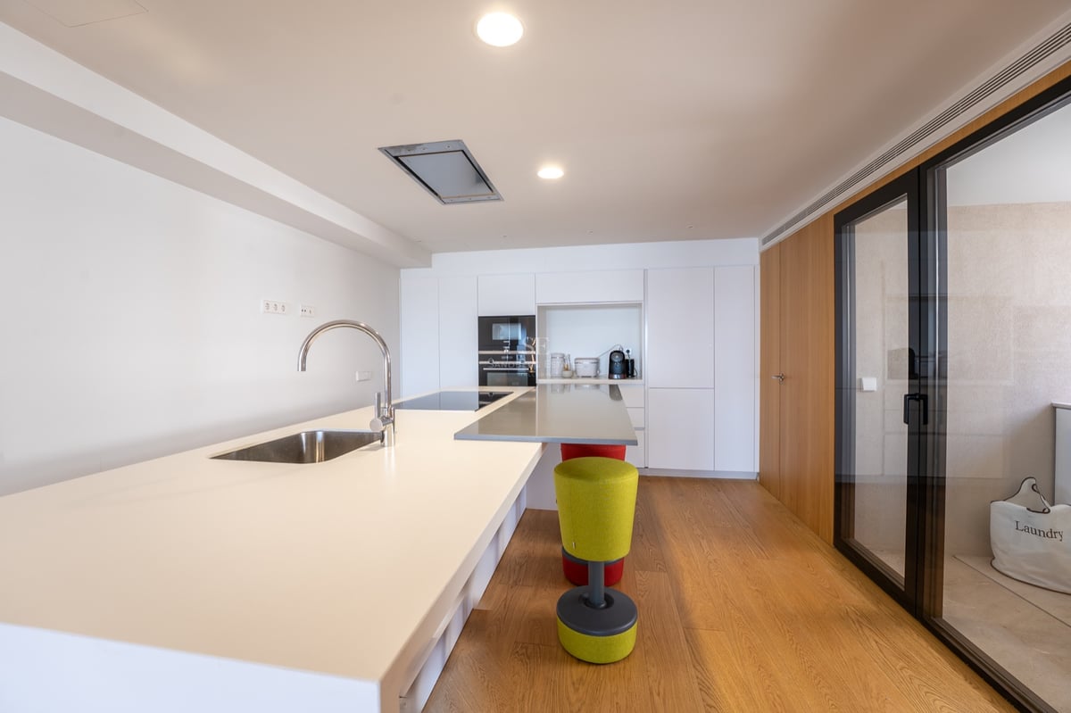 Ljust modernt kök med en stor vit köksö, diskho, trägolv och inbyggda vitvaror.