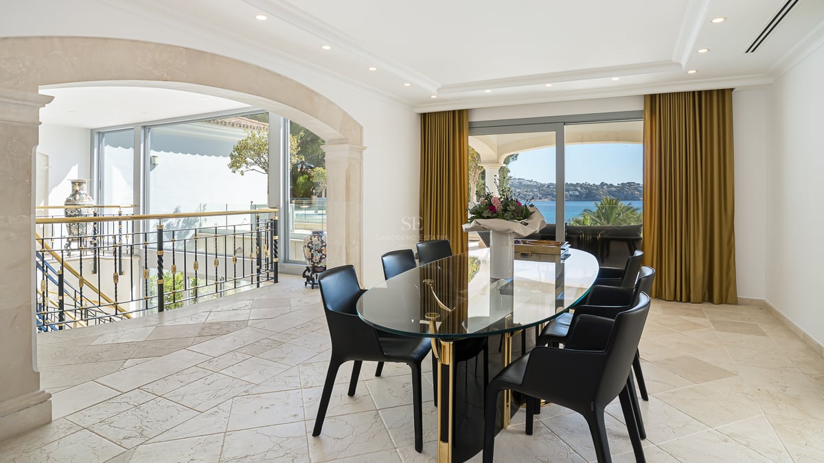 Moderner Essraum mit ovalem Glastisch, schwarzen Stühlen und großen Fenstern mit Blick auf das Mittelmeer.