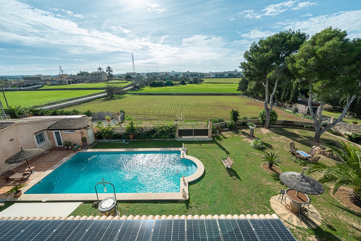 Vue d'en haut d'une piscine turquoise, jardin verdoyant et panneaux solaires surplombant la campagne méditerranéenne.