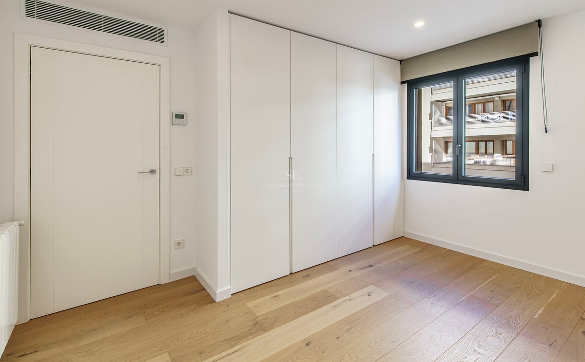 Chambre lumineuse avec parquet en bois clair, grands placards blancs intégrés et fenêtre au cadre sombre.
