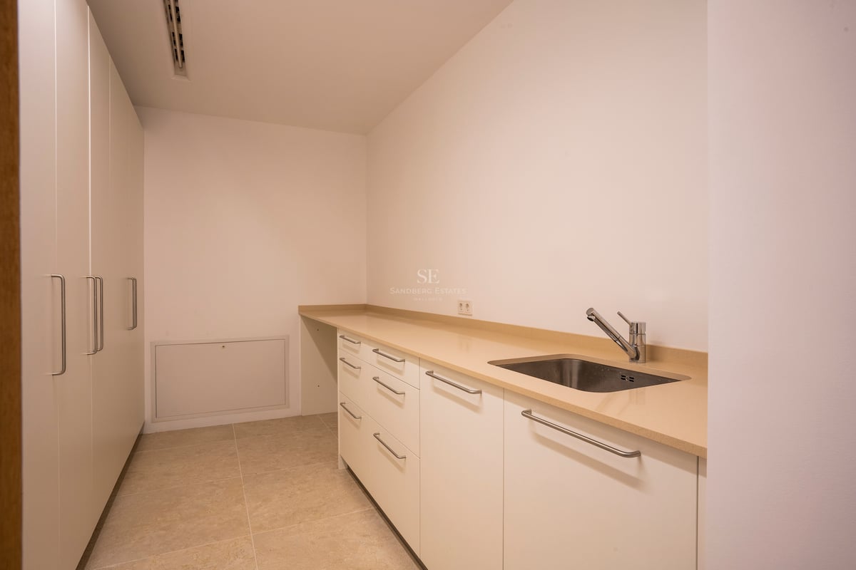 Weißer Wirtschaftsraum mit beiger Arbeitsplatte, Edelstahlspüle und deckenhohen Einbauschränken.