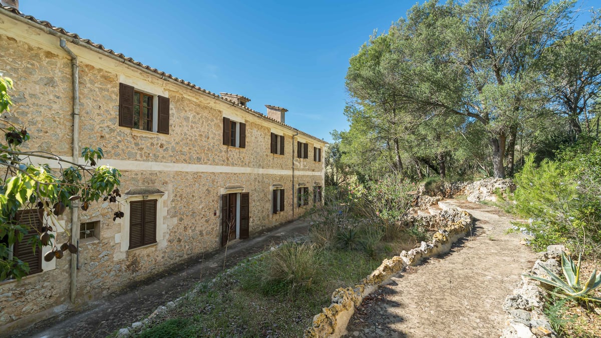 Un bâtiment rustique en pierre de deux étages avec des volets marron foncé entouré d'arbres verdoyants.