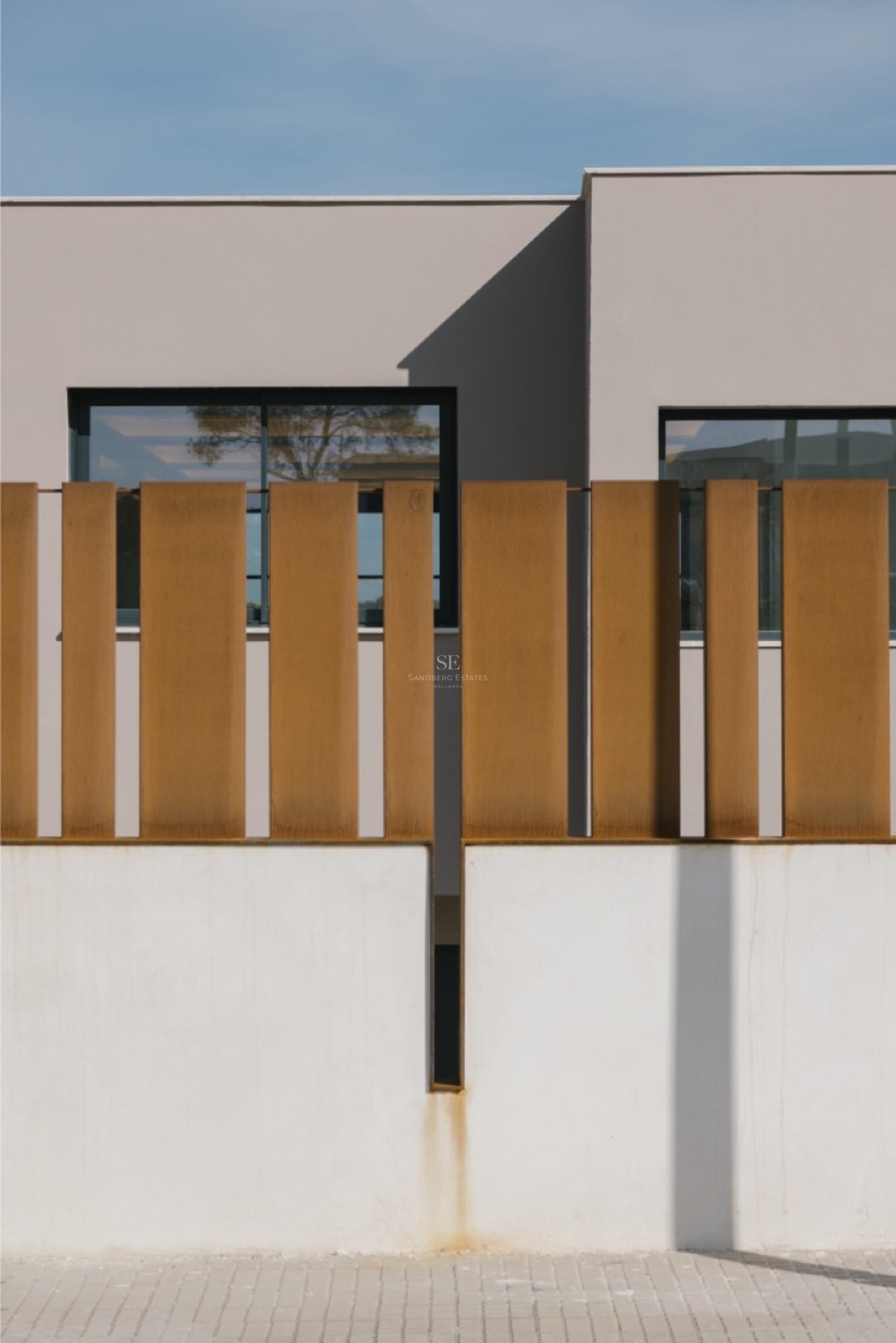 Weiße Begrenzungsmauer mit vertikalen Lamellen aus Cortenstahl und minimalistischer Fassade im Hintergrund.