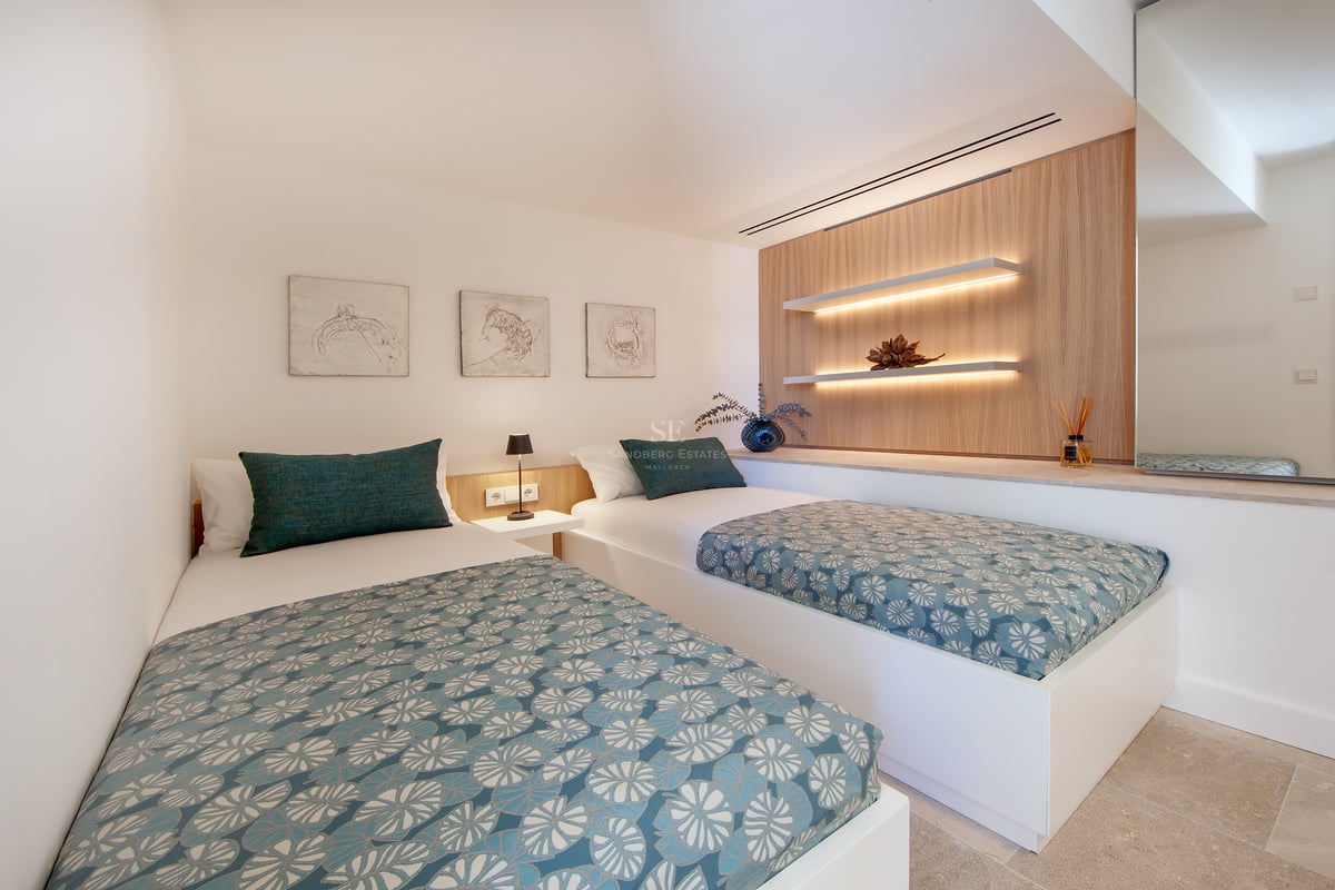 Chambre moderne avec deux lits simples, édredons à motifs bleu canard et étagères flottantes avec éclairage LED.