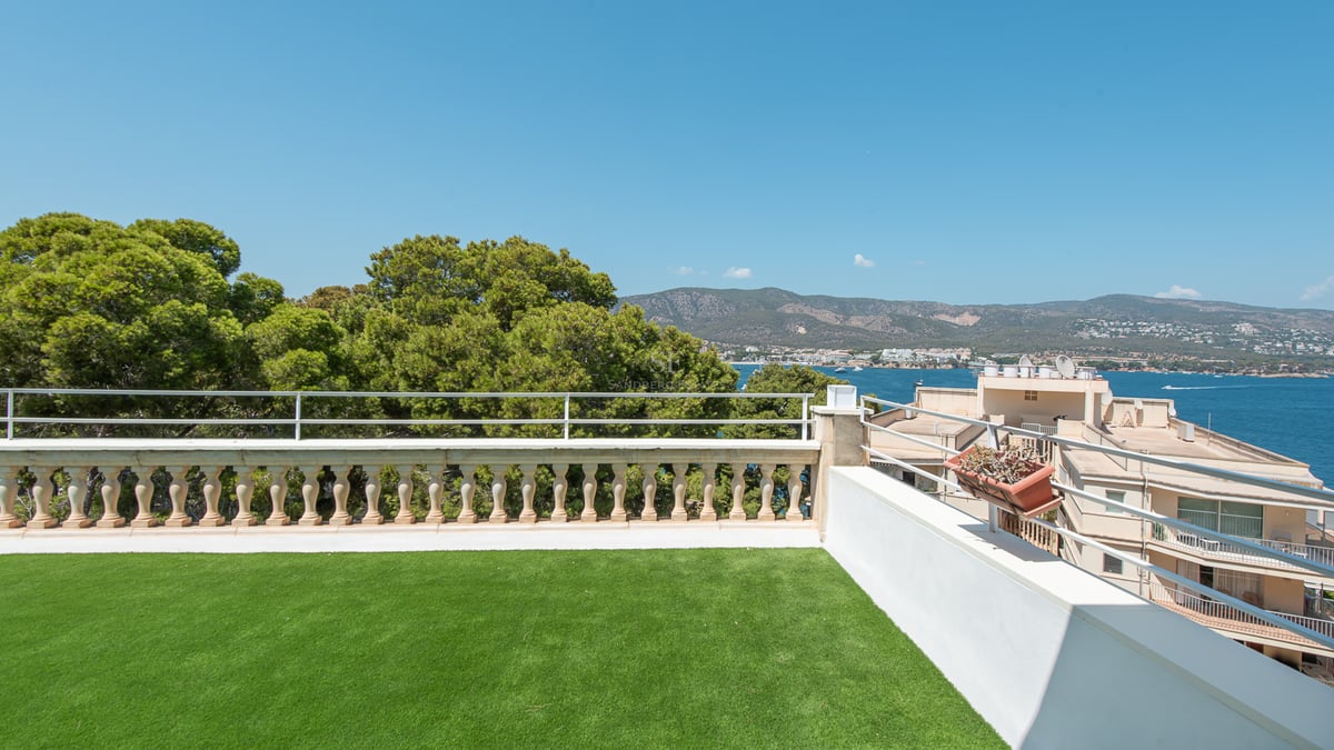 Terrasse avec gazon synthétique, balustrade en pierre et vue sur la Méditerranée et les montagnes environnantes.