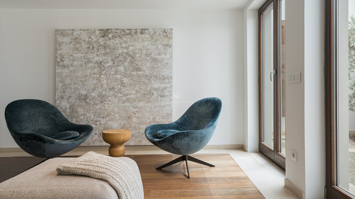 Deux fauteuils en velours bleu canard face à une grande toile abstraite à côté d'une baie vitrée toute hauteur.