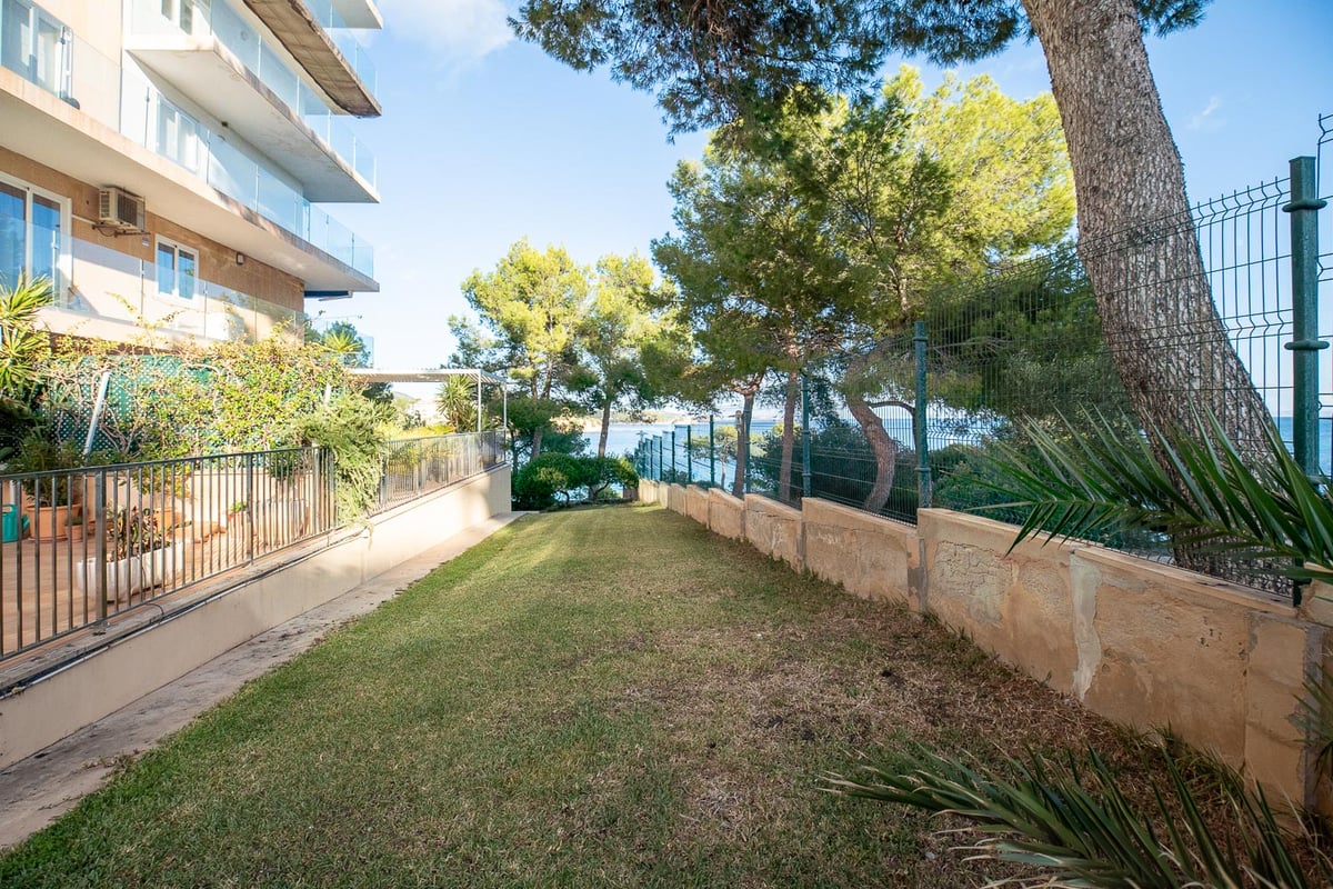 Gepflegte Rasenfläche neben einem modernen Gebäude mit Pinien und Meerblick im Hintergrund.