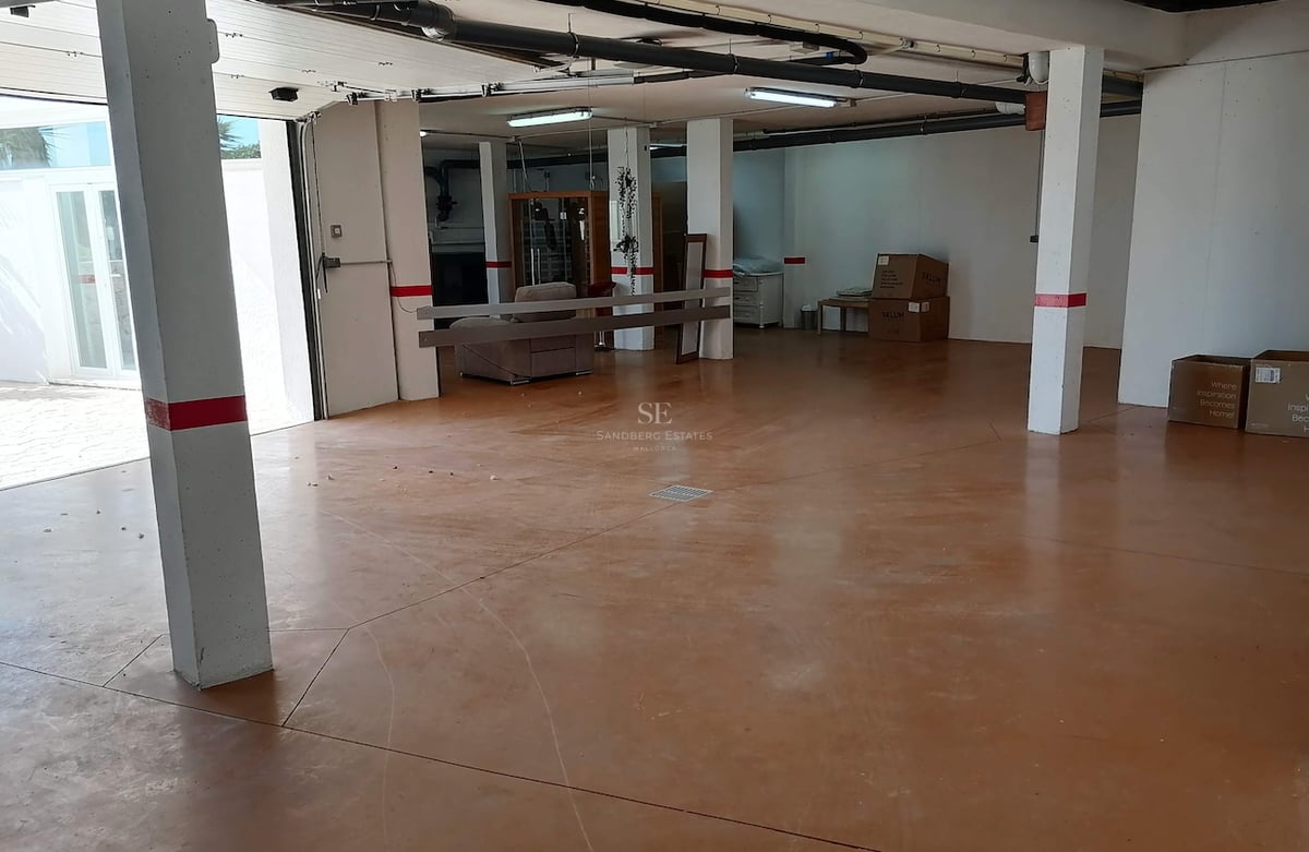 Vue intérieure d'un grand garage souterrain avec sol en époxy terre cuite, piliers blancs et tuyauterie apparente.