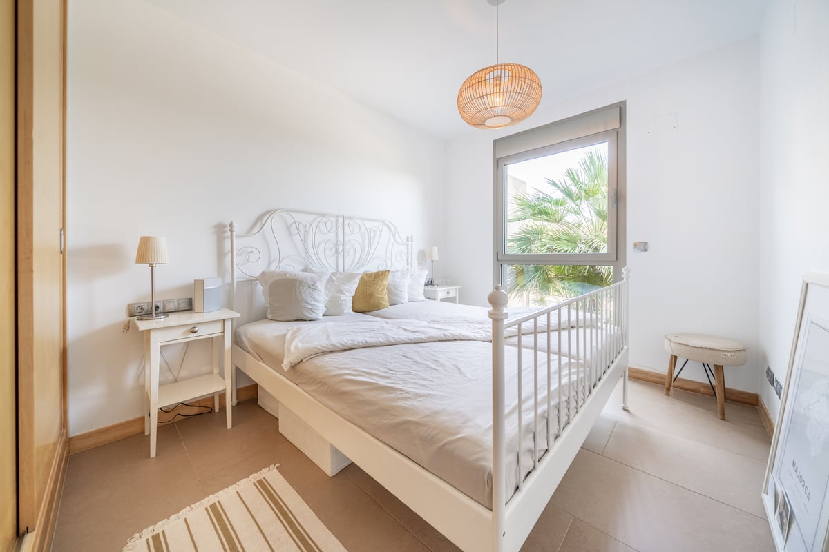 Chambre avec lit en fer blanc, armoire intégrée en bois et fenêtre donnant sur un palmier.