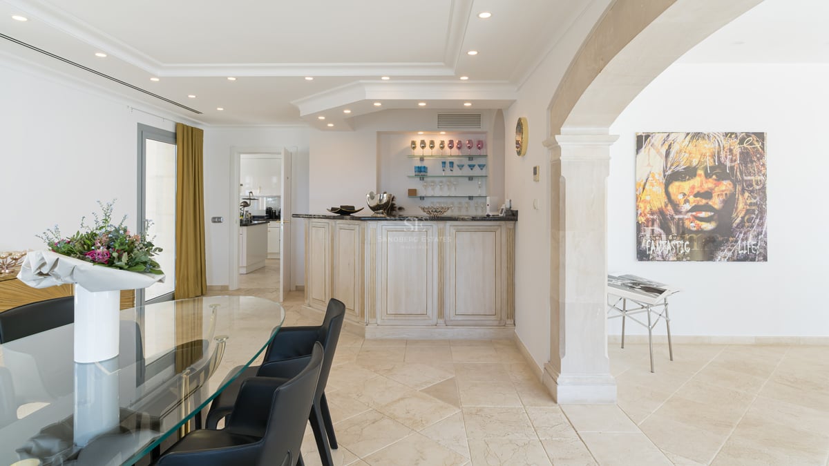 Modernes Esszimmer mit Glastisch, dunklen Stühlen, weißer Bar und klassischem Steinbogen.