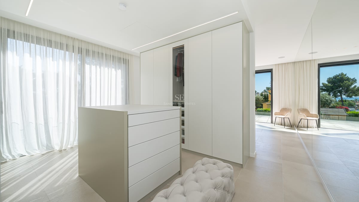 Dressing spacieux avec placards blancs, îlot central, pouf capitonné et vue sur mer par les grandes baies vitrées.