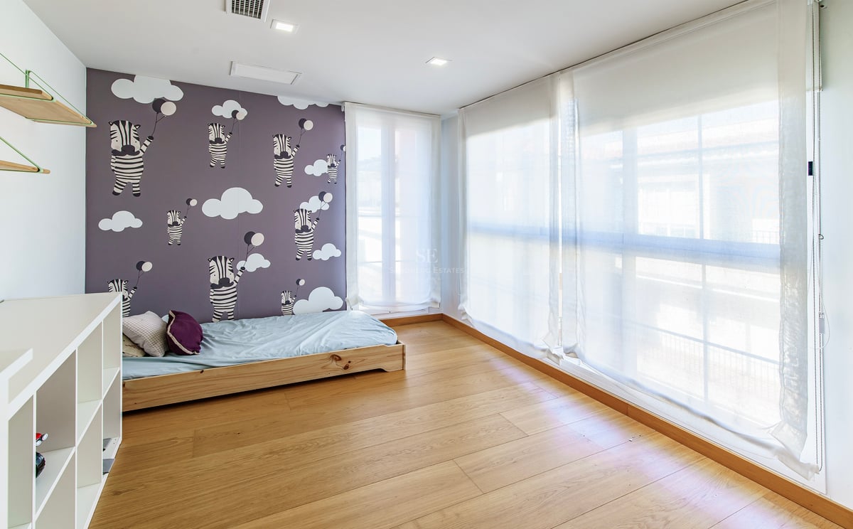 Ljust barnrum med zebramönstrad tapet, ljust trägolv och stora fönster med vita tunna gardiner.