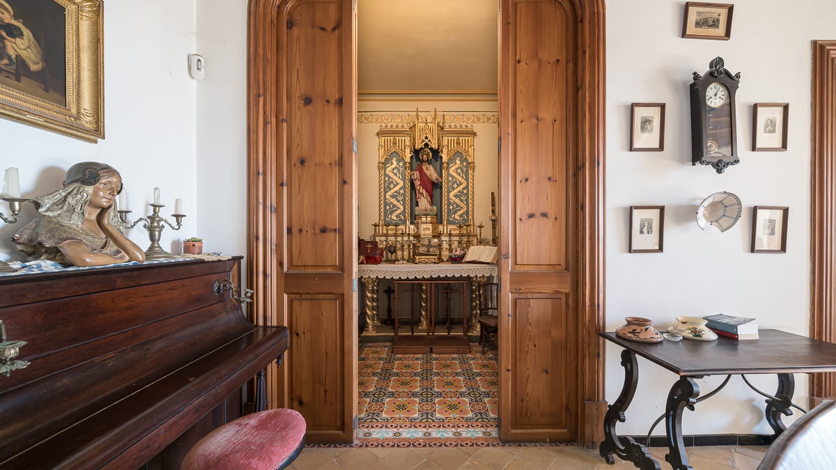 Vue à travers des portes en bois sur une petite chapelle privée ornée à côté d'un piano droit.