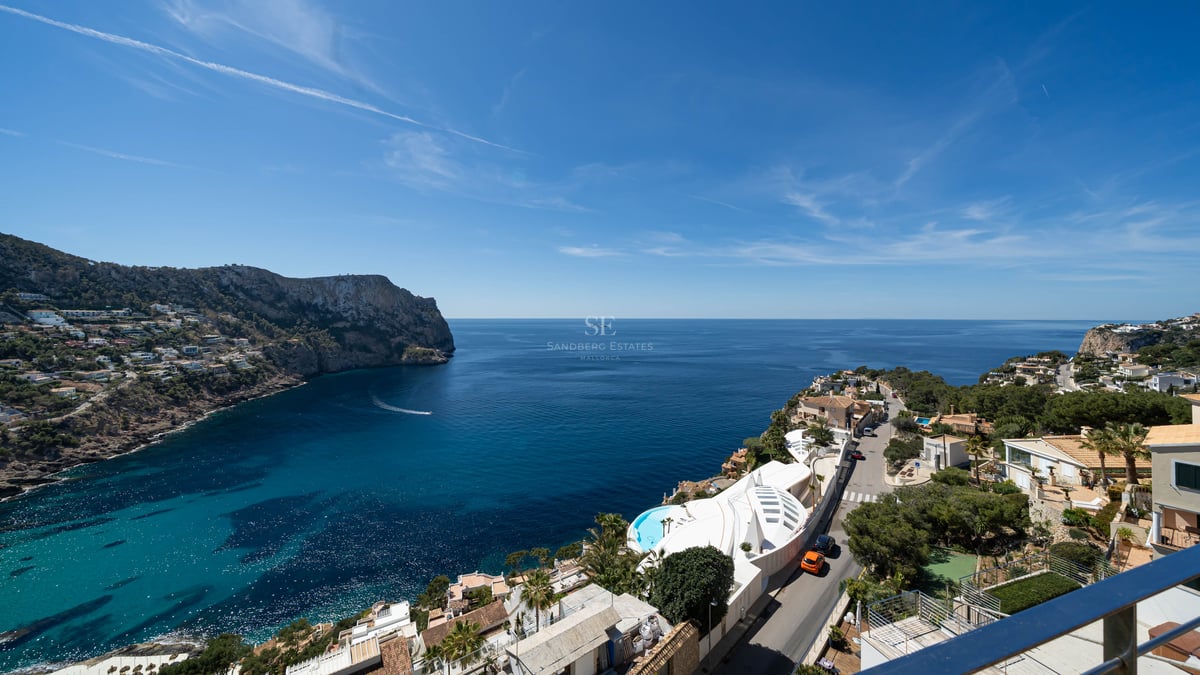High-angle view of a deep blue Mediterranean bay surrounded by rocky cliffs and coastal luxury villas under a clear sky.
