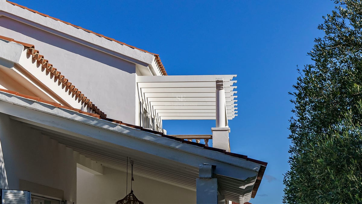 Vit villafasad med träpergola, terrakottatak och klarblå himmel på Costa del Sol.