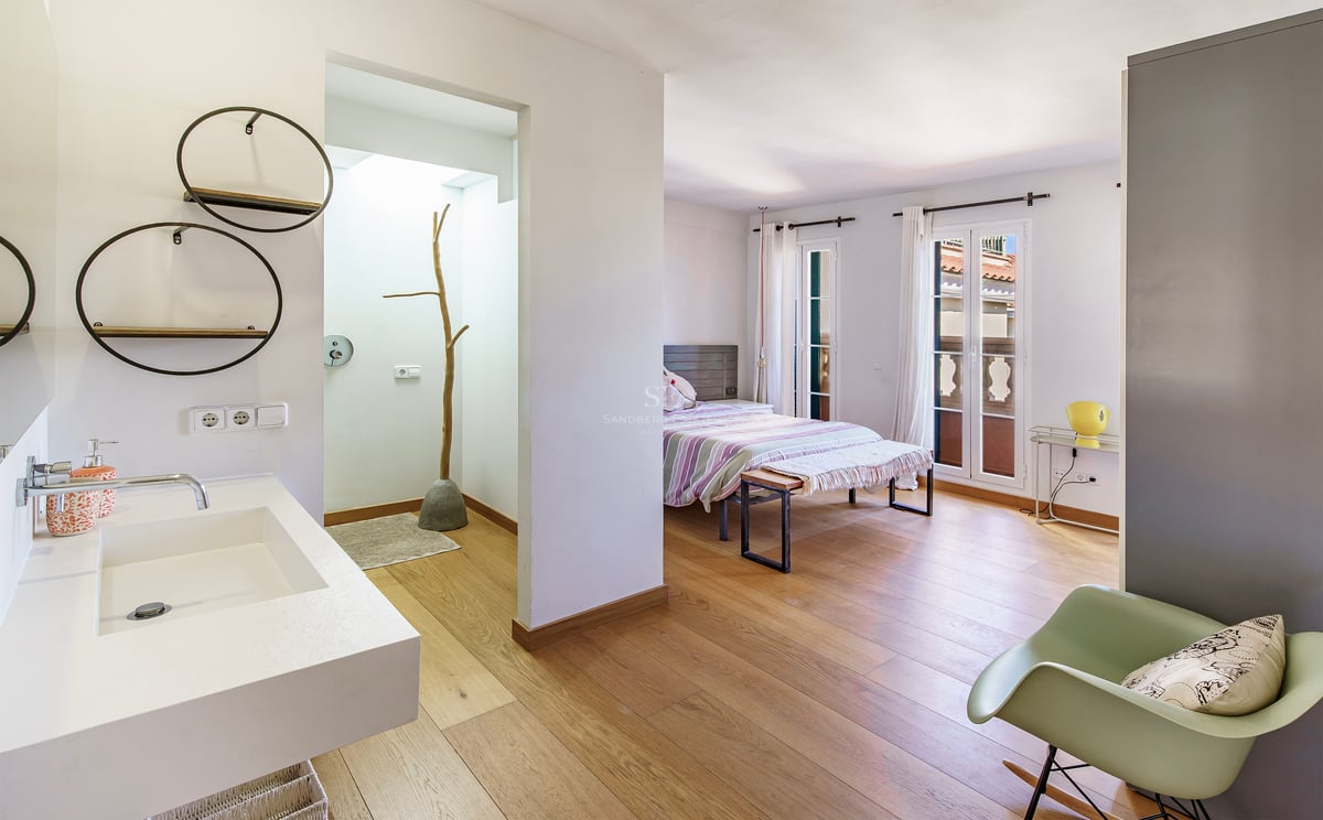 Rymligt sovrum med ljust ekparkettgolv och öppet badrum med modern vit kommod.