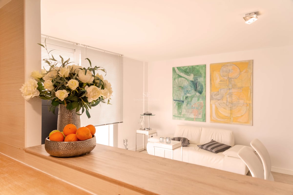 Helles Wohnzimmer mit weißem Ledersofa, abstrakten Gemälden und einer Holztheke mit Blumendekor.