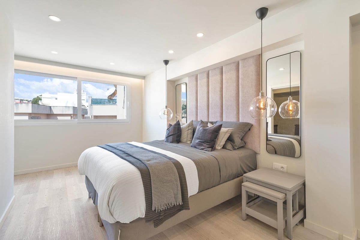 Zeitgenössisches Schlafzimmer mit gepolstertem Kopfteil, Glaspendelleuchten und hellem Holzboden.