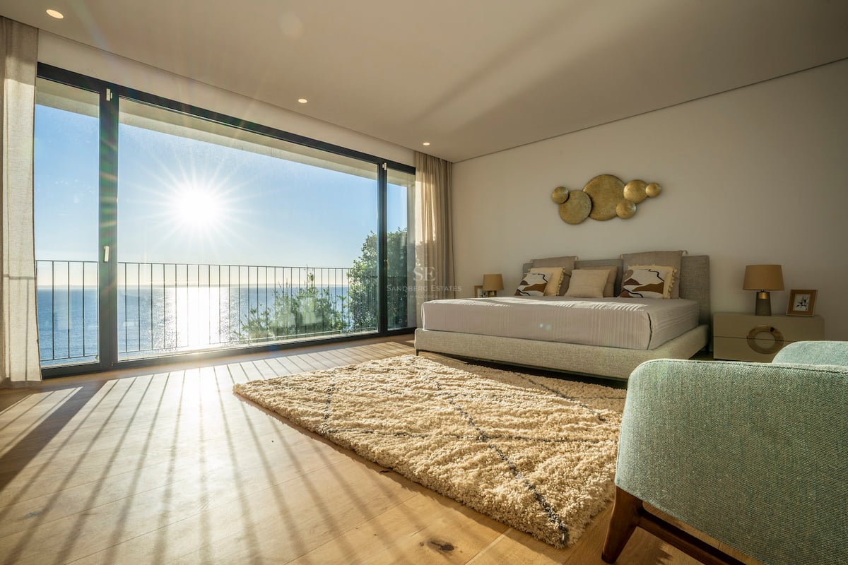 Helles Hauptschlafzimmer mit bodentiefen Glastüren, Eichenparkett und Terrasse mit Blick auf das blaue Meer.