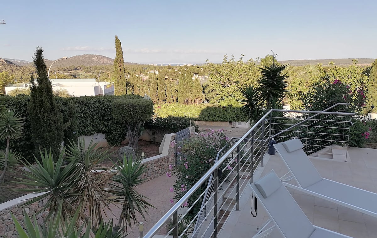 Une terrasse ensoleillée avec des chaises longues modernes et des garde-corps en acier inoxydable surplombant un jardin.