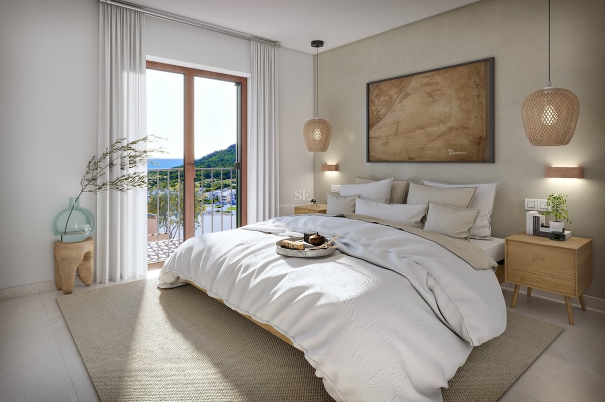 Bright bedroom featuring a white bed, wicker lamps, and a balcony with mountain and sea views.