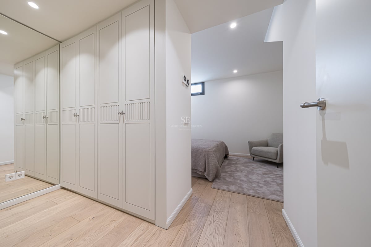 Cream lacquered built-in wardrobes with a full-length mirror and light oak flooring leading into a bedroom.