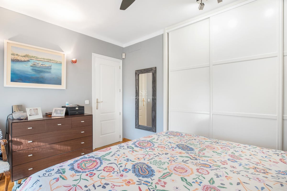 Helles Gästezimmer mit großen weißen Schiebetürenschränken, dunkler Holzkommode und geblümter Bettwäsche.