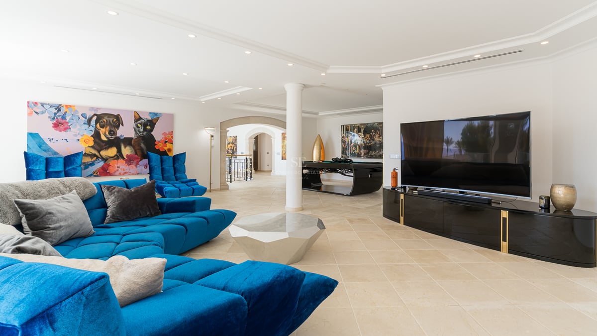 Heller Wohnraum mit blauem Samtsofa, geometrischem Couchtisch und Billardtisch im Hintergrund.