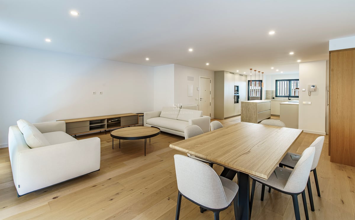 Pièce moderne spacieuse avec canapés blancs, grande table à manger en bois et cuisine contemporaine en arrière-plan.