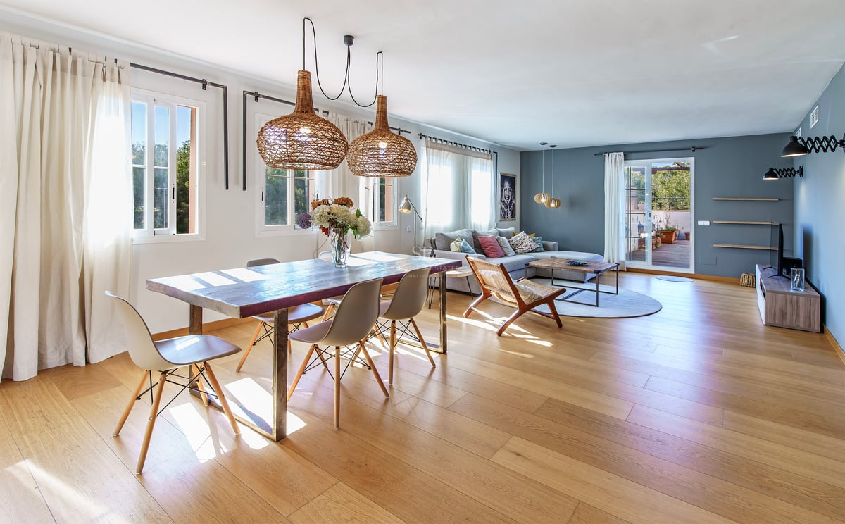 Ljust vardagsrum med ekparkett, rustikt matbord under flätade lampor och utgång till terrassen.