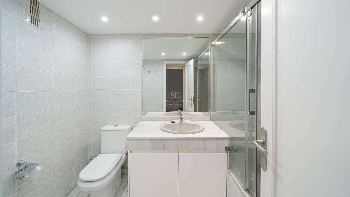 Ljust badrum med vit marmorkommod, duschvägg i glas och ljusgrått väggkakel.